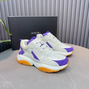 AMIRI Trainer replica sneakers in white, purple, and orange colorway, displayed on a gray surface with branded box in background, showcasing luxury sneaker design.