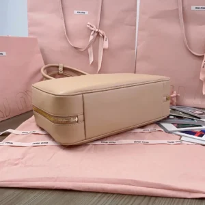 Miu Miu handbag large beige leather bag with gold zipper and rounded handles resting on pink fabric