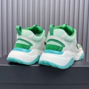 Amiri Trainer sneakers in white and green, showcasing the rear view with mesh and rubber detailing, displayed on a dark surface.