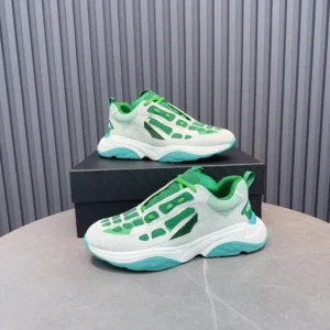 Amiri Trainer sneakers in green and white, displayed on a gray surface with a black box, showcasing a modern design and luxury appeal.