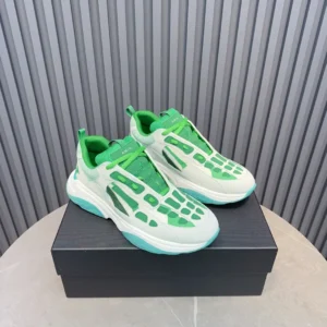 Amiri Trainer sneakers in green and white, displayed on a black box, showcasing modern design and vibrant color scheme, available for purchase.