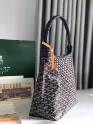 Goyard Hobo Boh è Me Stray Bag in brown patterned material, featuring a navy shoulder strap and orange tag, displayed on a countertop with elegant decor.