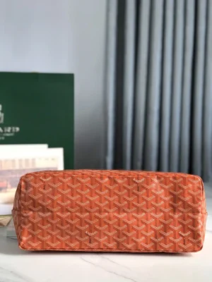 Goyard Hobo Boh è Me Stray Bag in orange, showcasing signature pattern and structure, placed on a marble surface with a green box and curtains in the background.