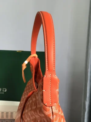 Goyard Hobo Boh è me Stray Bag featuring an orange shoulder strap and signature patterned fabric, displayed against a green background.