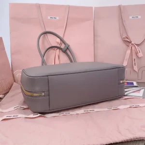 Miu Miu tote bag medium gray leather with gold zipper and dual top handles on pink cloth and bags background