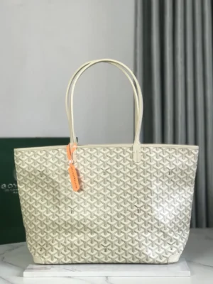 Goyard White Tote Bag featuring a textured design, dual handles, and an orange tag, displayed on a marble surface against a neutral background.