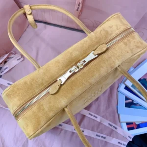 Miu Miu new arrival briefcase in deer velvet leather with gold zipper, showcasing a multi-functional design, placed on a pink background with fashion elements.