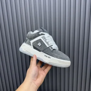 AMIRI Trainer sneaker in gray and white, held in hand, showcasing luxury design and brand logo.