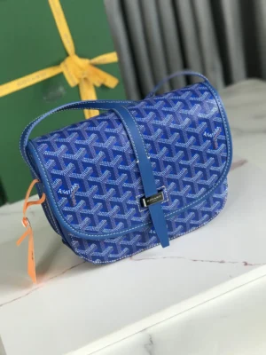 Goyard Belvedere 2nd Generation Bag in blue, featuring a crossbody design with a narrow buckle, leather border, and adjustable shoulder strap, displayed on a marble surface with a green gift box in the background.