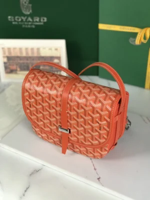 Goyard Belvedere II Bag in orange with signature pattern, featuring a narrow buckle closure and adjustable shoulder strap, displayed on a marble surface alongside matching silk ribbon gift packaging.