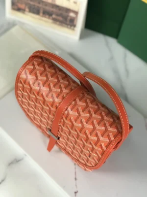 Goyard Belvedere II Bag in orange, featuring a woven pattern, leather strap, and metallic buckle, displayed on a marble surface with a green box backdrop, emphasizing luxury and practicality.