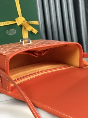 Goyard Belvedere II Bag interior showcasing orange leather lining and pockets, with matching silk ribbon gift packaging in background.