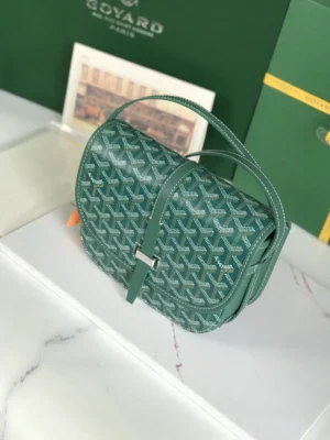 Goyard Belv é d è re 2 green crossbody bag with silk ribbon, featuring a minimalist design, adjustable shoulder strap, and signature pattern, displayed on a marble surface with packaging in the background.