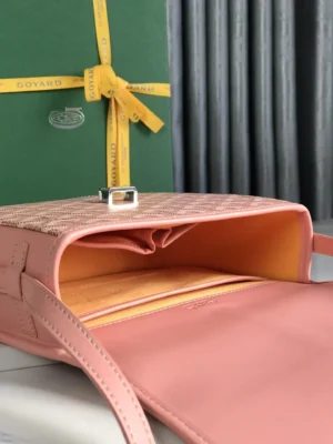 Metallic leather crossbody shoulder purse by Goyard, featuring a pink exterior, open interior with orange lining, and signature buckle detail, displayed alongside branded packaging.