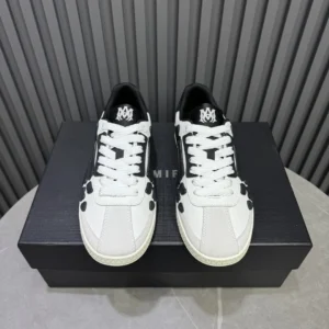 AMIRI Trainer sneakers in black and white, displayed on a black box, showcasing luxury footwear design and branding.