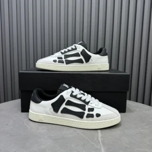 AMIRI Trainer sneakers in white and black design, displayed on a gray surface with a black box, showcasing luxury footwear style.