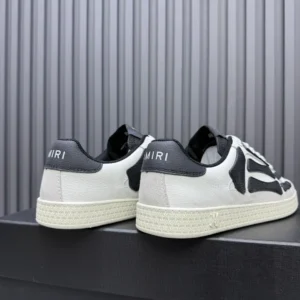 AMIRI Trainer sneakers featuring a black and white design, showcasing the brand logo on the heel, set against a textured background.