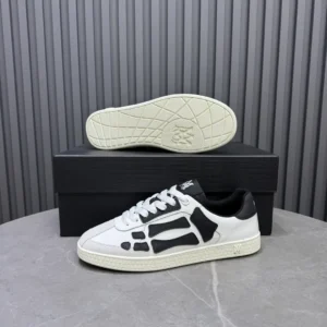 AMIRI Trainer sneakers in white and black, displayed on a gray surface with a black box, showcasing unique design elements and luxury branding.