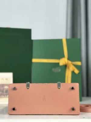 Goyard Sa ï Gon Bag in soft pink leather with signature G logo, displayed alongside green gift box with yellow ribbon, emphasizing luxury craftsmanship and design.