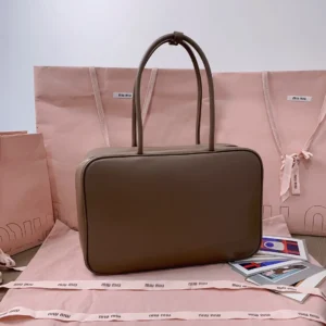 Handmade spliced leather briefcase by MIU MIU, featuring a smooth, delicate finish, displayed on pink branded packaging, emphasizing its multifunctional design and stylish appeal.