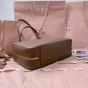 Handmade spliced leather briefcase in smooth brown leather, featuring a gold zipper, displayed on a pink fabric background with MIU MIU shopping bags.