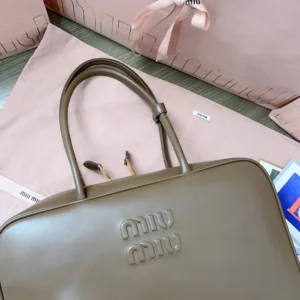 Handmade spliced leather briefcase by MIU MIU, featuring smooth brown leather, embossed logo, and soft cotton satin lining, displayed with original packaging.