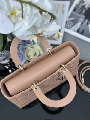 Dior Book Tote Bag in refined leather with iconic wicker stitch, featuring detachable shoulder straps and D.I.O.R. pendant, displayed with flowers and stylish background.
