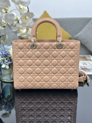 Dior Book Tote Bag in soft pink leather with iconic quilted design, featuring dual top handles and detachable shoulder strap, elegantly displayed on a reflective surface with floral accents.
