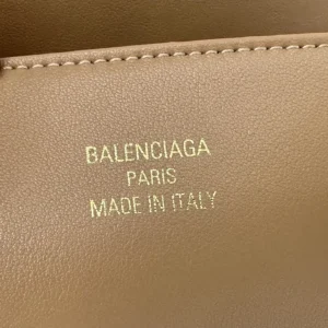 Balenciaga logo embossed in gold on a beige leather handbag, showcasing luxury craftsmanship and designer branding.