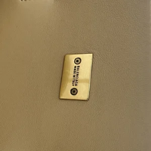 Balenciaga logo plaque on a beige handbag, emphasizing luxury and designer branding for the trending IR handbag.