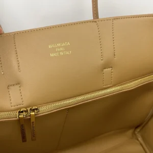 Interior view of Balenciaga handbag featuring embossed logo, zippered compartment, and beige leather lining, highlighting luxury craftsmanship and design.