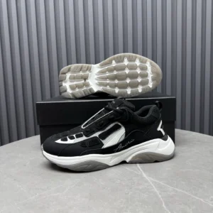 AMIRI Trainer sneaker in black and white, showcasing unique design elements and sole, placed on a marble surface with a black box in the background.