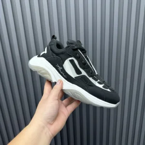 AMIRI Trainer sneaker in black and white, held in hand, showcasing premium design and athletic style.