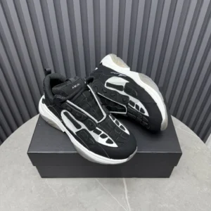 AMIRI Trainer sneakers in black and white, displayed on a black box against a textured background, showcasing luxury design and style.