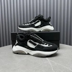 AMIRI Trainer sneakers in black and white, showcasing a stylish design with unique detailing, displayed on a minimalist surface with a box.