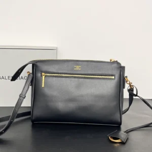 Balenciaga Small Mailman Crossbody Bag in black leather with gold hardware, featuring a front zip pocket and adjustable strap, displayed against a neutral background.
