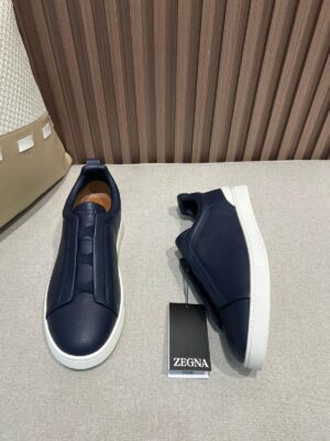 Minimalist navy leather slip-on shoes by Zegna displayed on a neutral background, featuring a clean design, elastic hidden panel, and lightweight rubber sole.