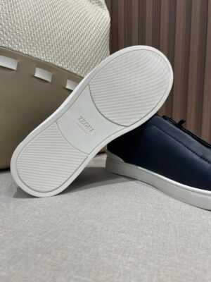 Navy leather slip-on shoes by Zegna with a white rubber sole, showcasing minimalist design and premium craftsmanship, set against a textured background.