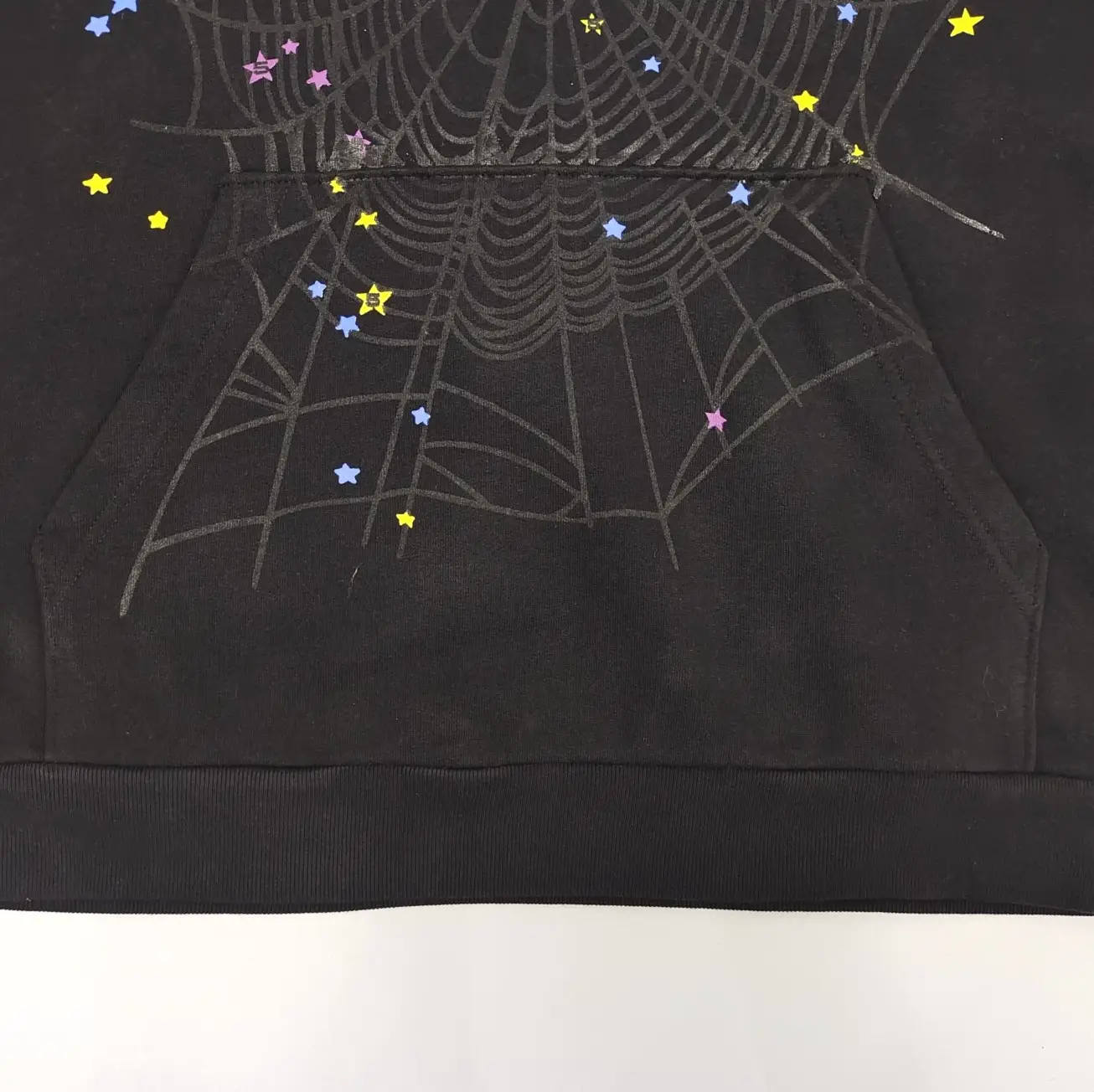 No visible brand or product model details, black fabric with spiderweb and colorful star design print on sweatshirt material