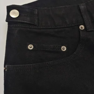 The image shows black denim fabric with metal rivets, but no brand or product details are visible to create the requested alt text.