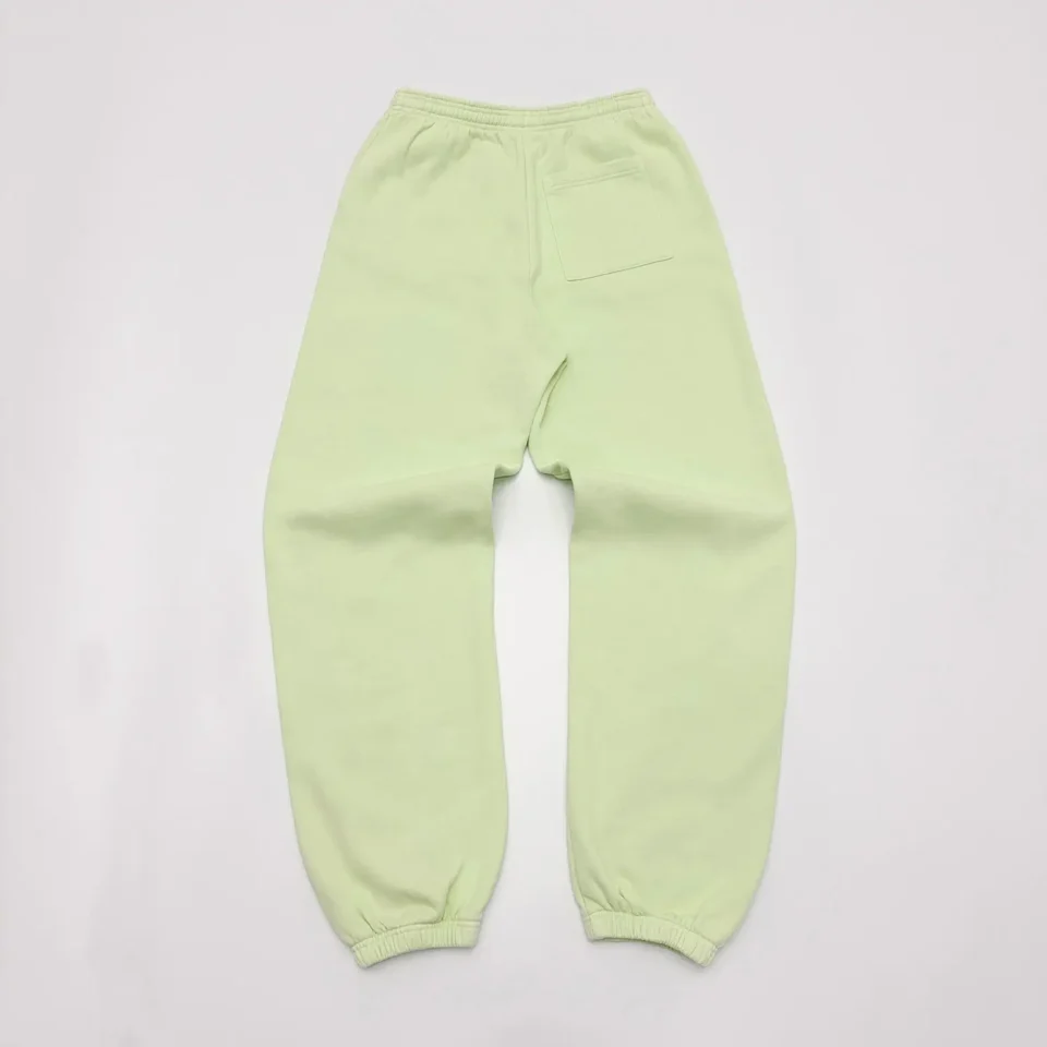 The image shows a light green bottom wear, likely sweatpants, laid out flat on a white surface. The pants have an elastic waistband, elastic cuffs at the ankles, and a single pocket on the back right side. The fabric appears to be soft and comfortable, suitable for casual wear or loungewear. Would you like me to generate an SEO-optimized alt text for this item based on the described attributes? If so, please provide the brand name and model if available.