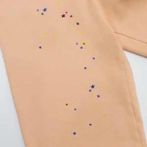 Sp5der Orange Pink Star Pants featuring colorful star embellishments on a peach fabric background.