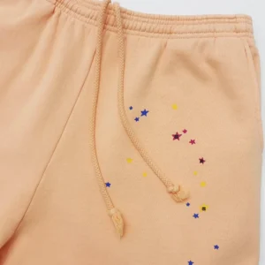 Sp5der Orange Pink Star Pants featuring a peach fabric with colorful star prints and drawstring detail.