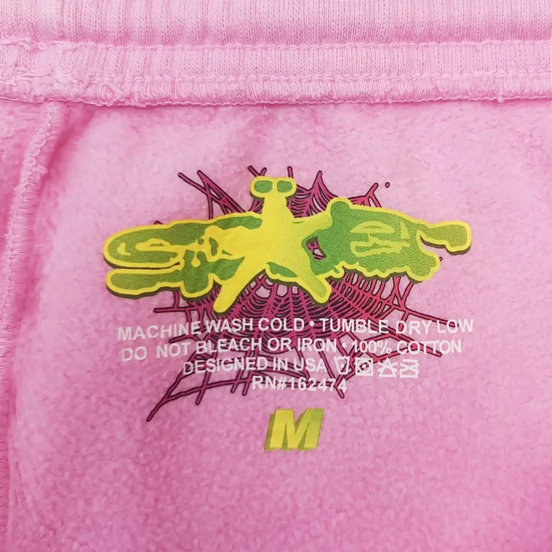 No brand or product type visible, pink cotton fabric with yellow and green graphic and size M label