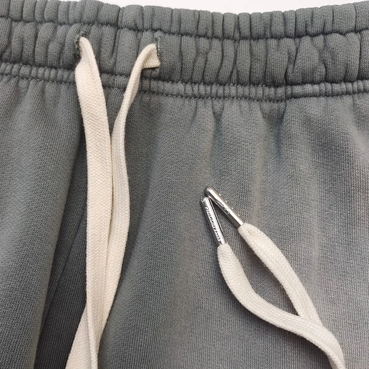 Unknown brand grey sweatpants close-up with white drawstrings and metal aglets textile material