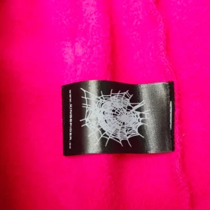 Label featuring spider web design on bright pink fabric, related to SP5DER SDER Rose Red White Legacy Pants.