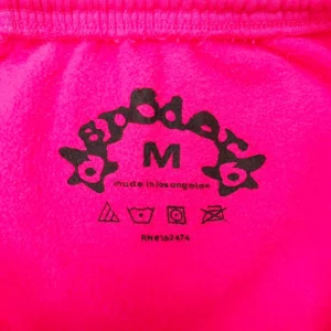 SDER Rose Red White Legacy Pants tag featuring brand logo, size M, and care instructions on vibrant pink fabric.