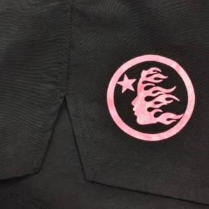 No visible brand or product name; close-up of black fabric with pink circular logo featuring a star and face with flame hair design on cotton material clothing