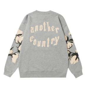 Gray hoodie featuring "another country" text and floral design on sleeves, from Denim Tears collection, showcasing trendy fashion style.