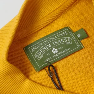 Denim Tears knitwear label green cotton tag on yellow fabric garment close-up